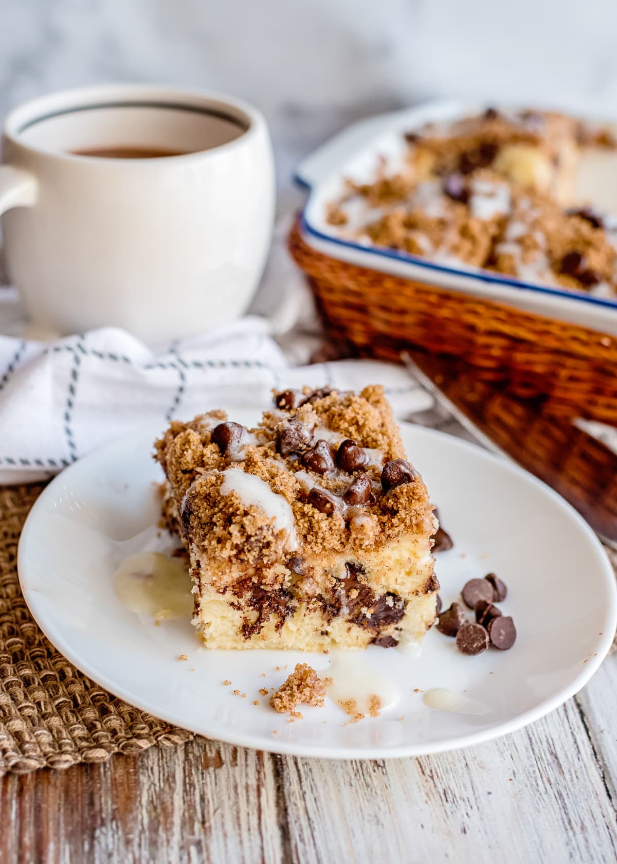 chocolate chip coffee cake on a white plate with a coffee mug in background.