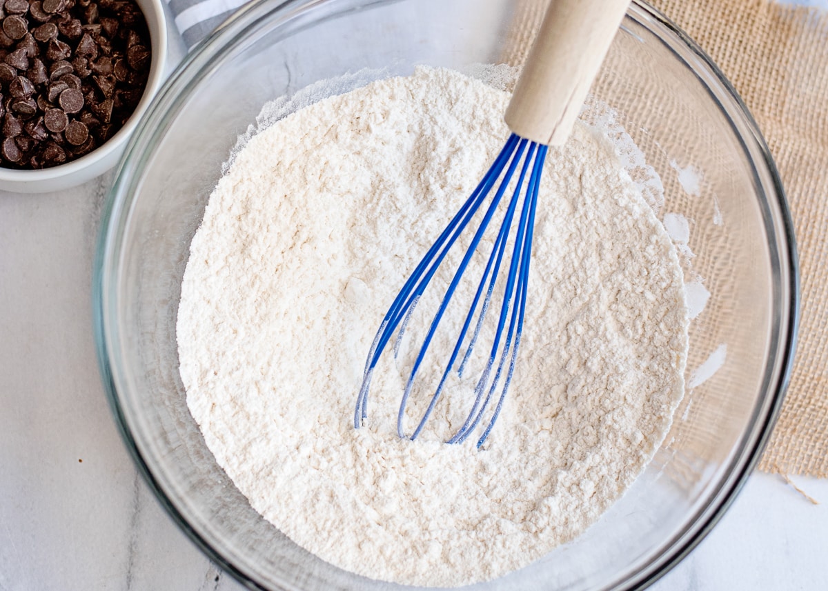 dry ingredients for cake in a glass bowl with a blue whisk.