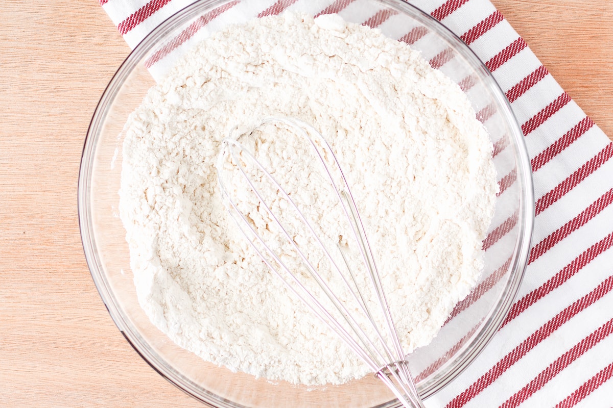 dry ingredients for cookies in a glass bowl with a whisk on top of a white and red striped napkin.