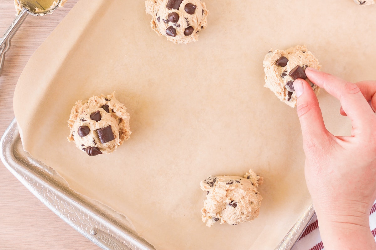 raw peanut butter chocolate chip cookie dough on a baking sheet with hand placing more chocolate chips on top.