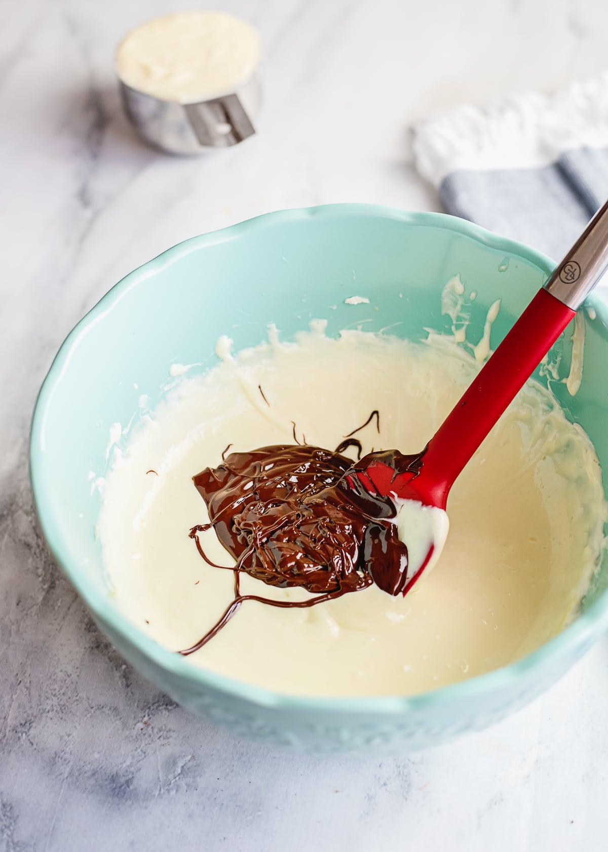 vanilla cream cheese mixture in a teal bowl with some chocolate mixed in.