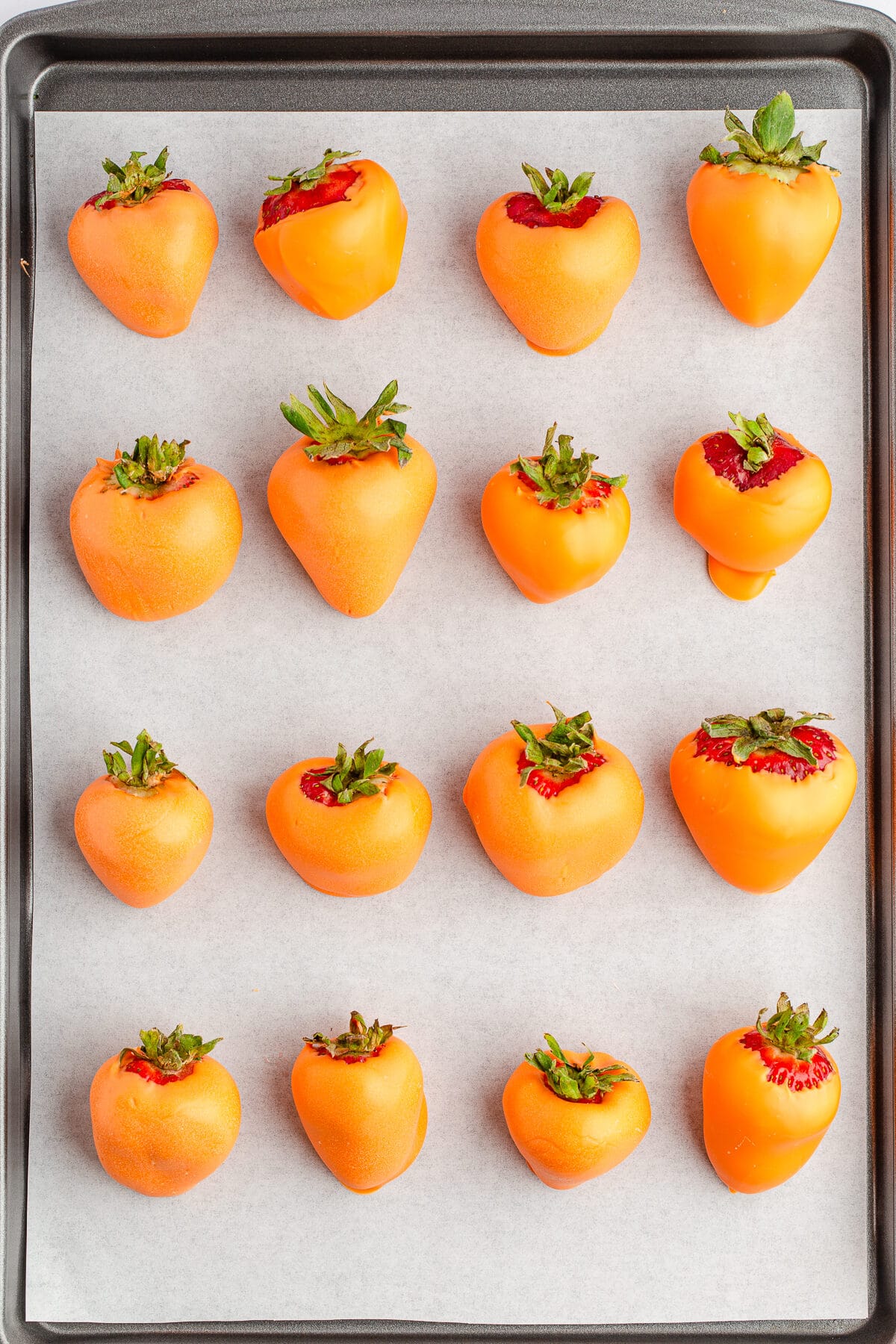 orange chocolate covered strawberries on a baking sheet lined with parchment paper.