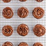 chocolate cream cheese frosting on cupcakes on a cooling rack.