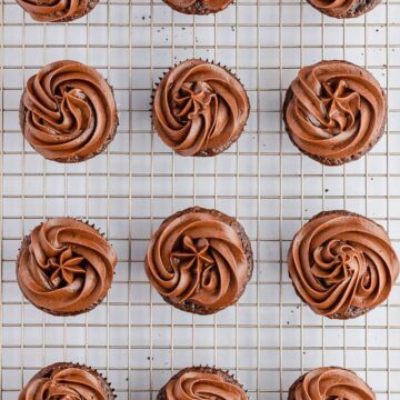chocolate cream cheese frosting on cupcakes on a cooling rack.