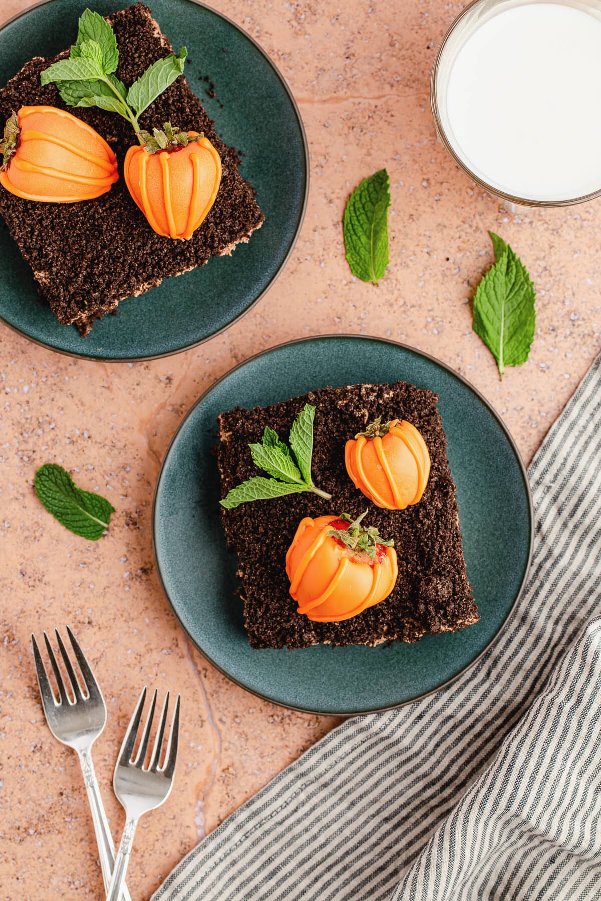 a slice of dirt cake on two teal plates topped with 2 chocolate covered strawberries that look like pumpkins.