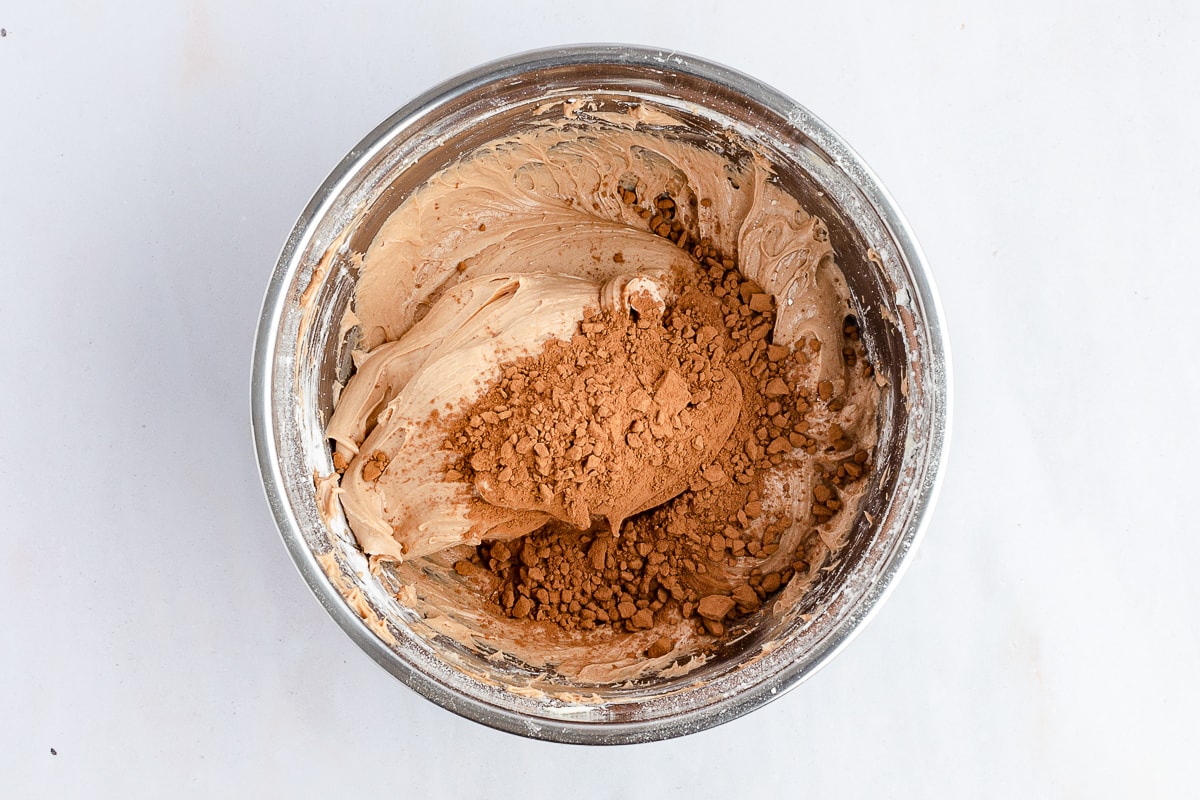 cocoa powder added to chocolate frosting in a bowl.