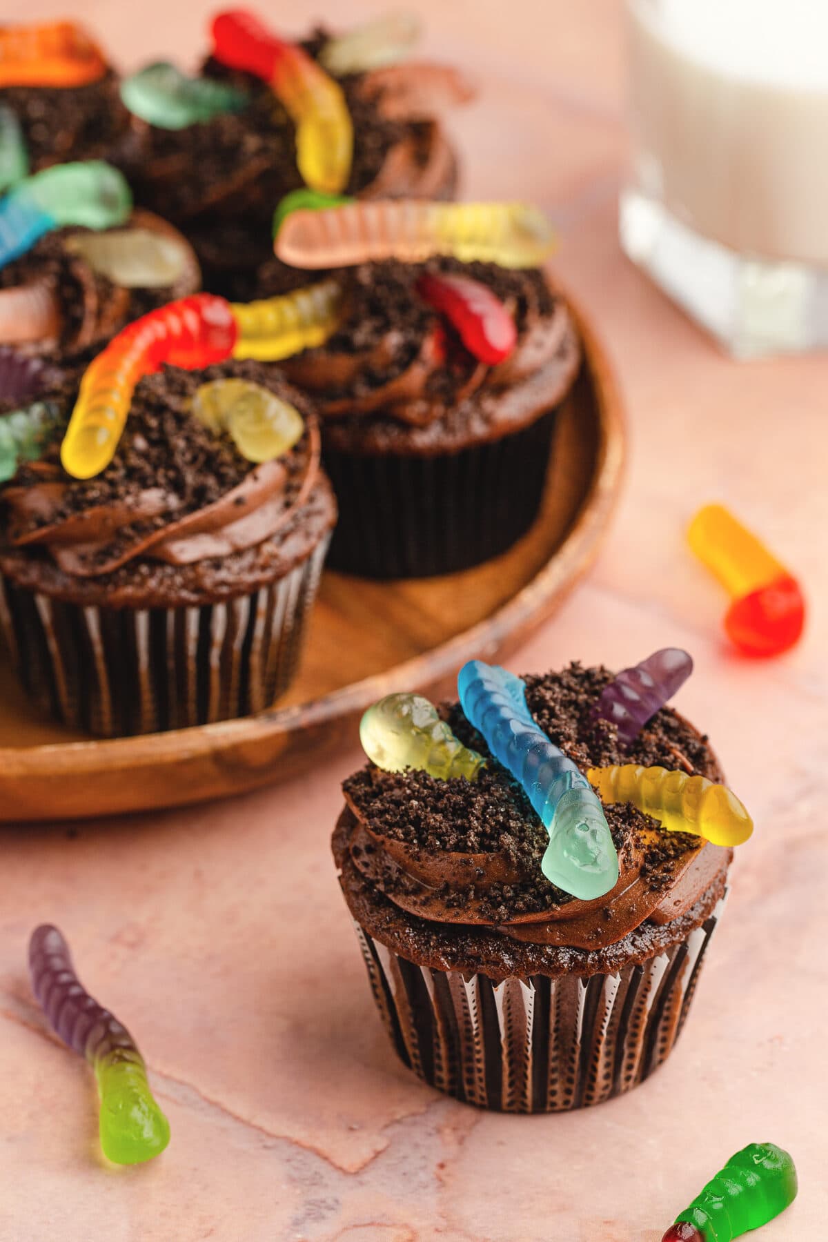 dirt cupcake with gummy worms on a terra cotta background with a plate full of dirt cupcakes in the background.