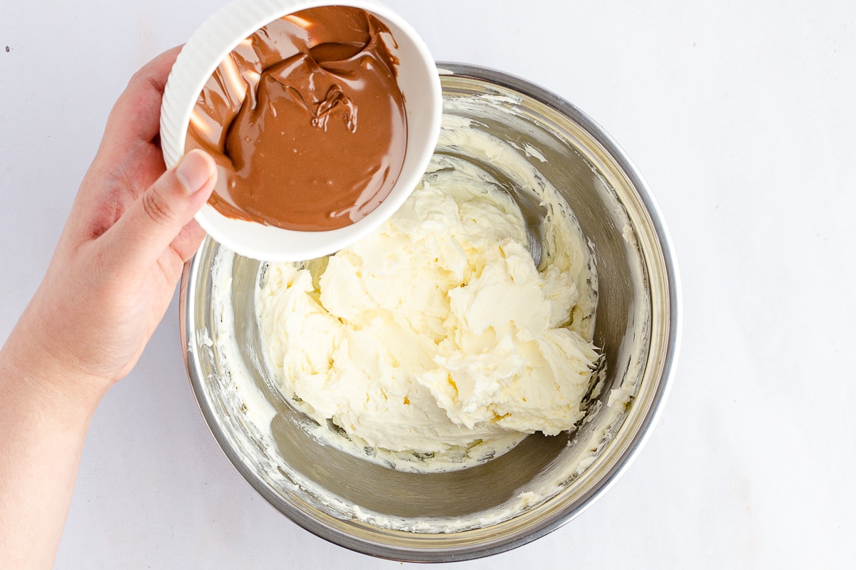 hand holding melted chocolate over a bowl with mixed cream cheese and butter.