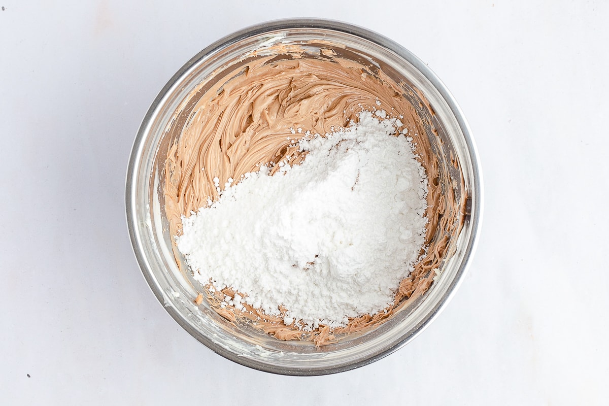 powdered sugar added to chocolate frosting in a bowl.