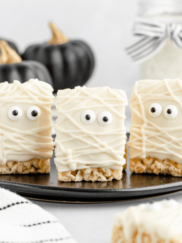 halloween mummy rice krispie treats on a black plate with one on the backdrop below the plate.