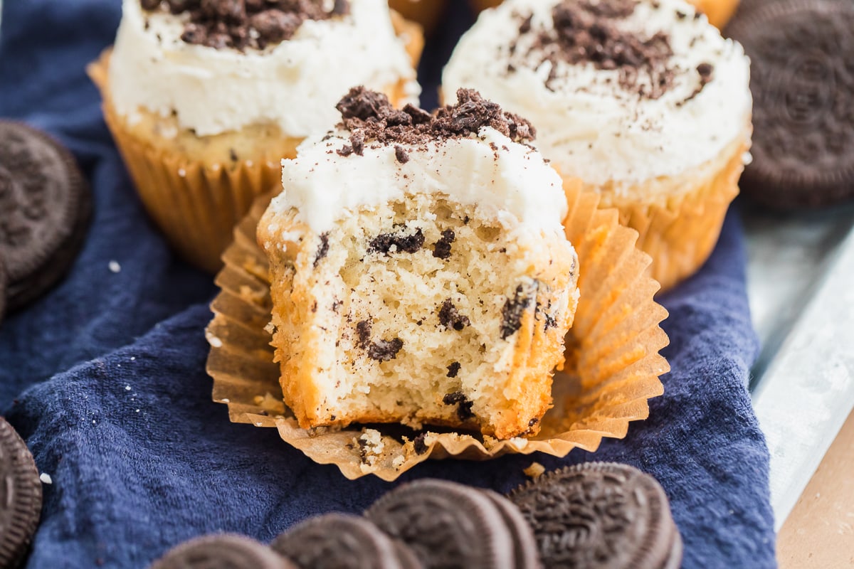 oreo cupcakes with vanilla buttercream and crushed oreos with bite taken out of one.
