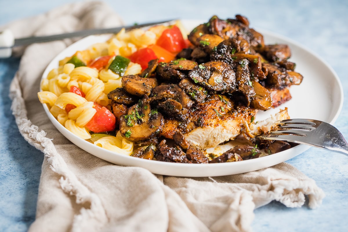 chicken and mushrooms cooked on a plate with pasta with tomatoes and zucchini.