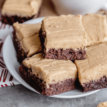 frosted coffee brownies on a white plate stacked.