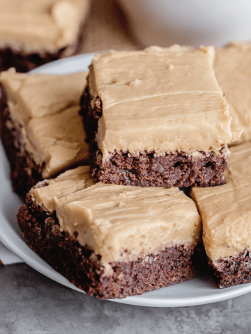 frosted coffee brownies on a white plate stacked.