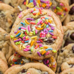 close up of sprinkle chocolate chip cookies on top of other cookies in three rows.