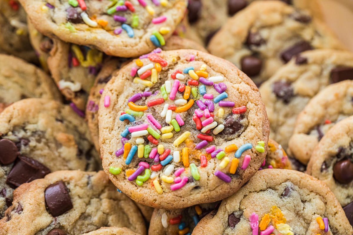 close up of a sprinkle chocolate chip cookie on top of other cookies in a row.