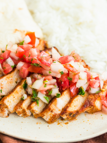 taco pork chops sliced with fresh pico de gallo on top served with rice and a tortilla on a beige plate.