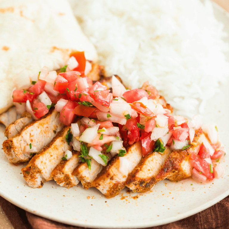 taco pork chops sliced with fresh pico de gallo on top served with rice and a tortilla on a beige plate.