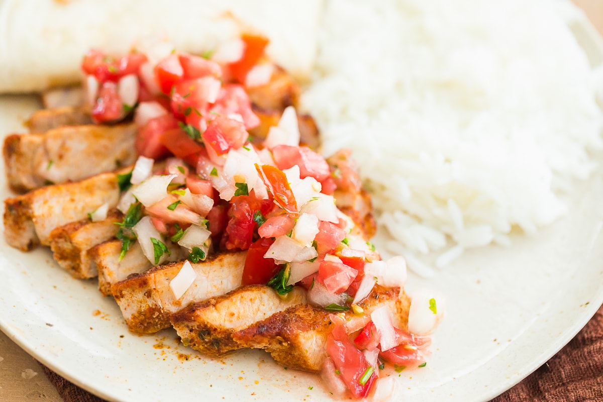 seasoned taco pork chops topped with fresh pico de gallo with white rice on a beige plate.