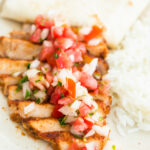 taco pork chop sliced with pico de gallo on top served with rice and a fresh tortilla on the side on a beige palte.