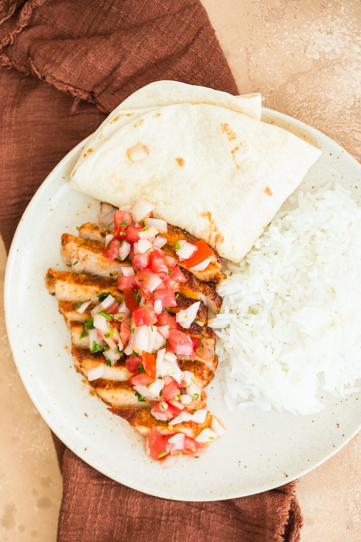 seasoned taco pork chops topped with fresh pico de gallo with white rice and a tortilla on a beige plate.