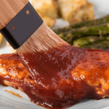 bbq sauce being spread on a piece of bbq chicken with a food safe brush.