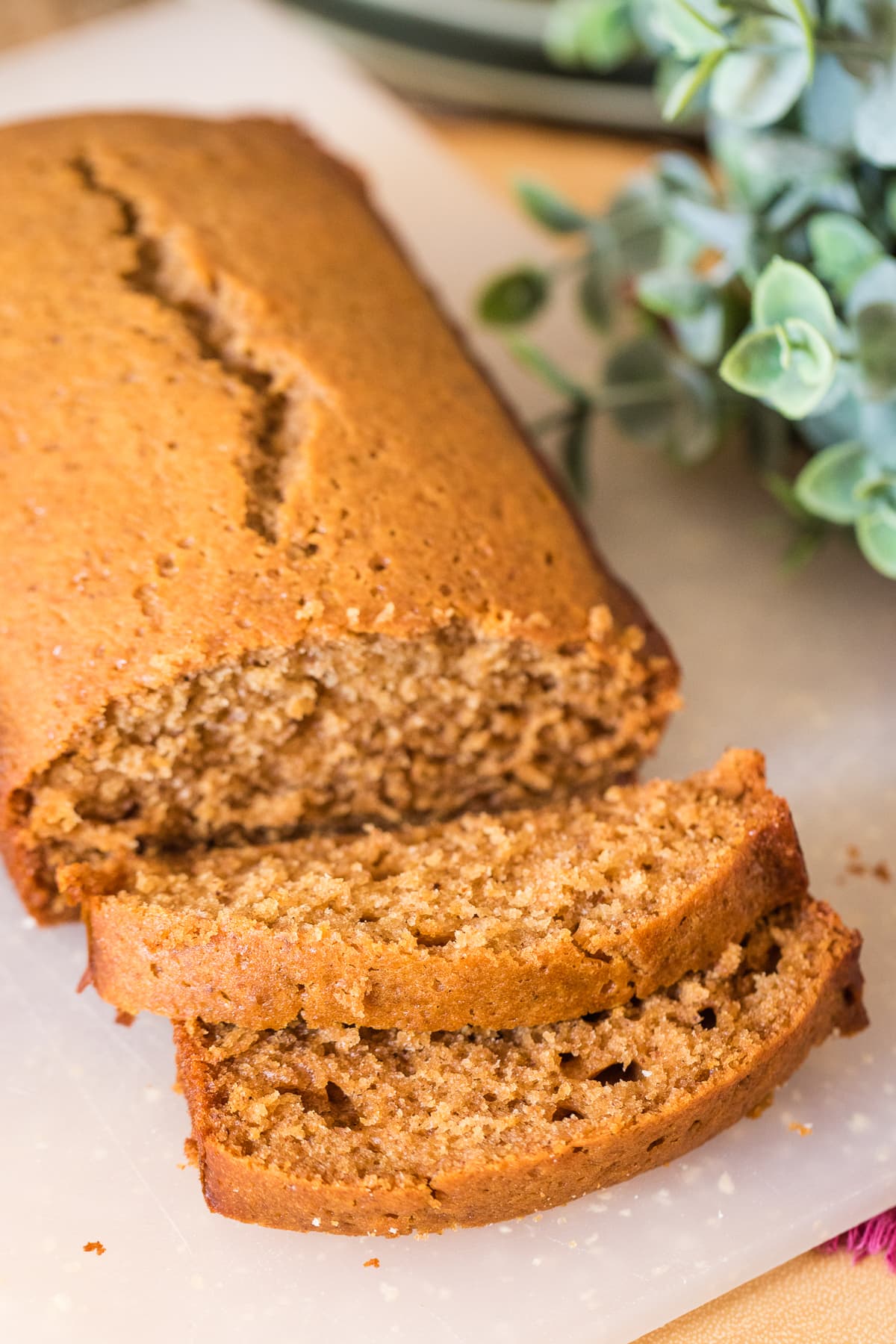 honey cake loaf with two slices on a cutting board with greenery to the right.