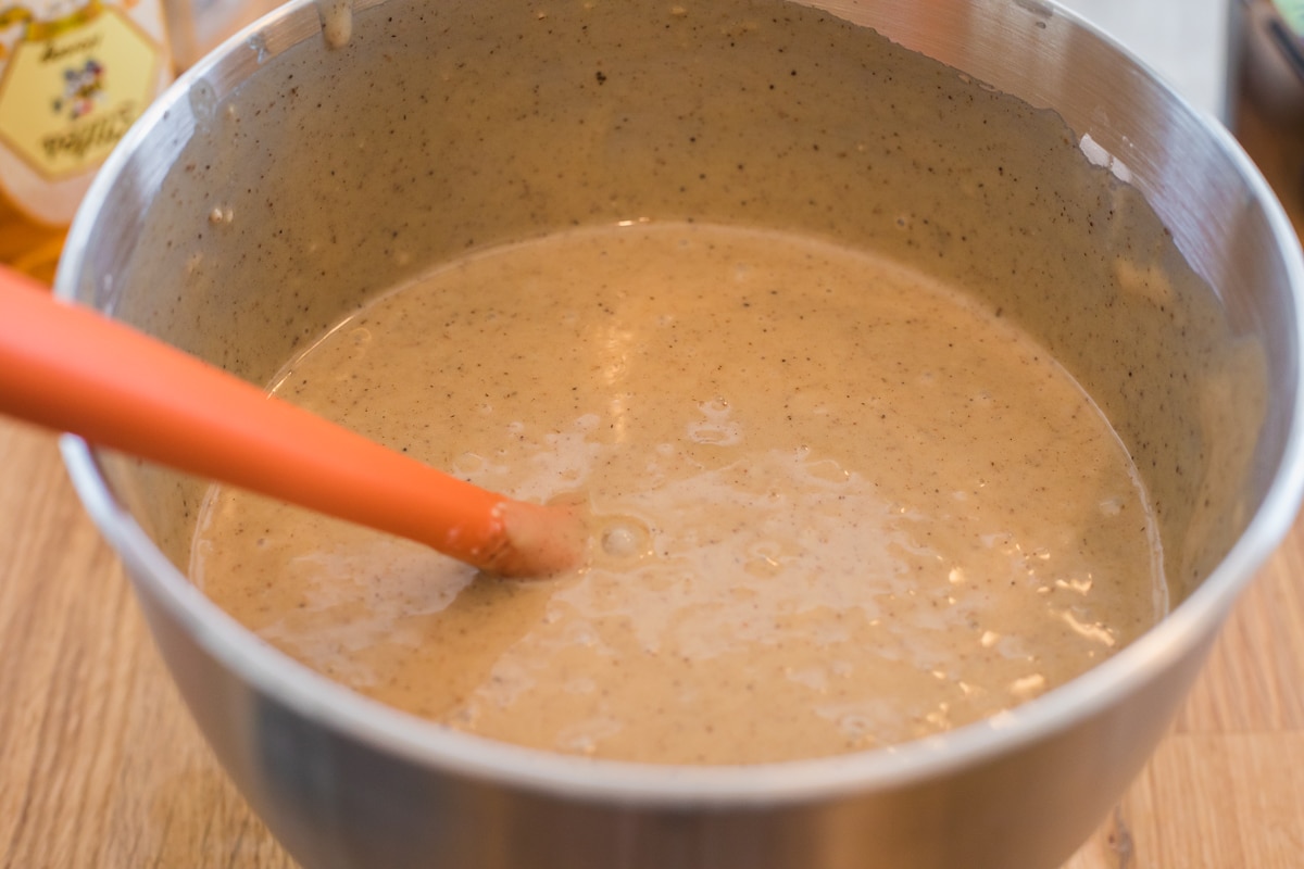 honey cake batter in a mixing bowl with an orange spatula.