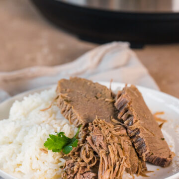 bottom round roast slices on a plate with rice and parsley garnish in front of the instant pot.