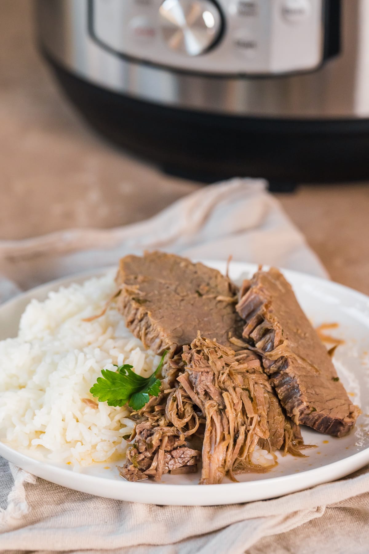 bottom round roast slices on a plate with rice and parsley garnish in front of the instant pot.