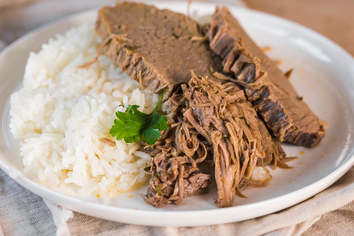 close up photo of instant pot bottom round roast on a white plate with white rice.