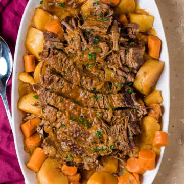 sliced Jewish brisket on a white platter with carrots and potatoes.