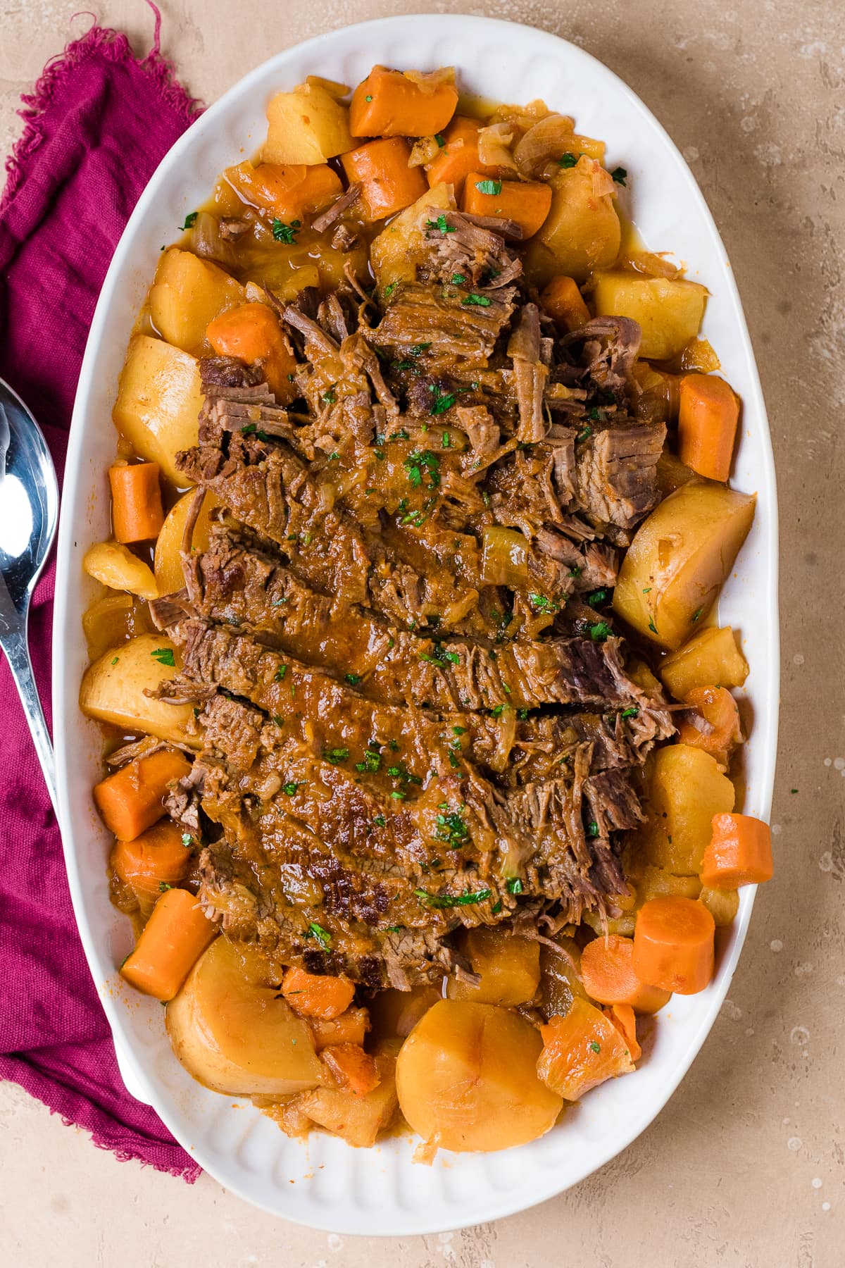 sliced Jewish brisket on a white platter with carrots and potatoes.