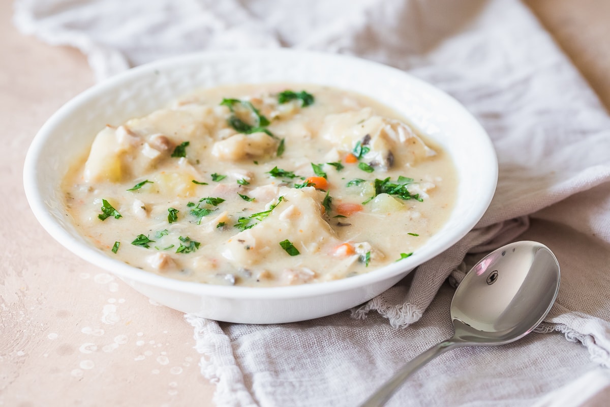 instant pot chicken and dumplings in a white bowl with a spoon to the lower right on with a beige napkin.