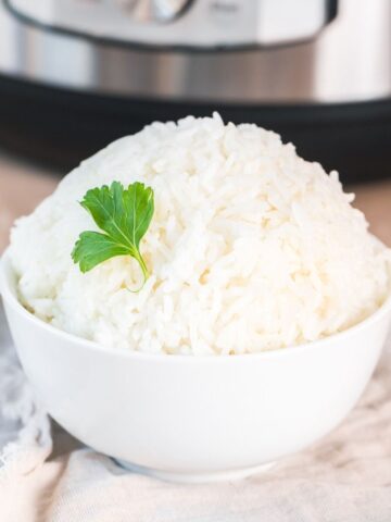 instant pot white rice in a white bowl with a garnish of parsley in front of an instant pot.