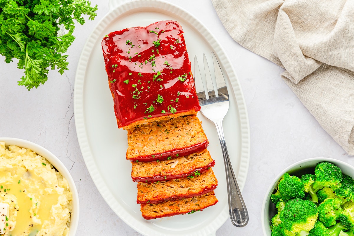 chicken meat loaf half sliced on a white platter with a serving fork to the right.