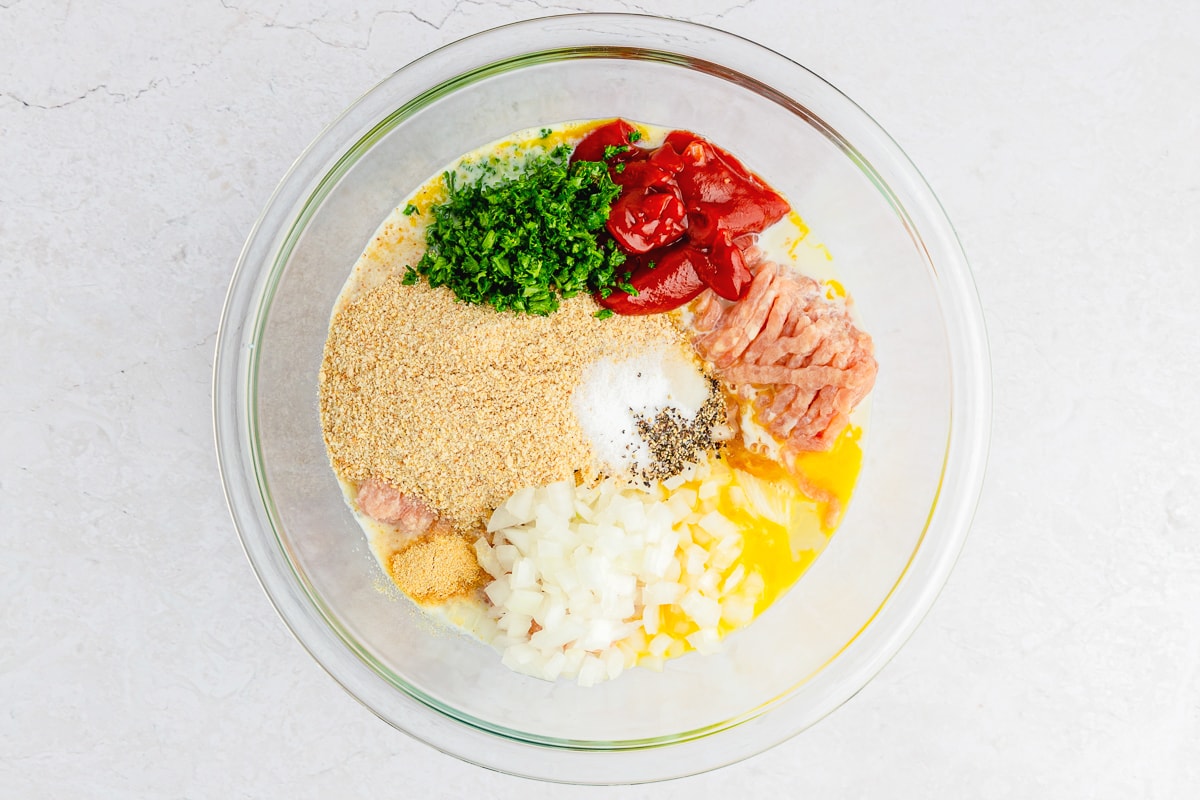 ground chicken and other ingredients in a glass bowl to make meatloaf.