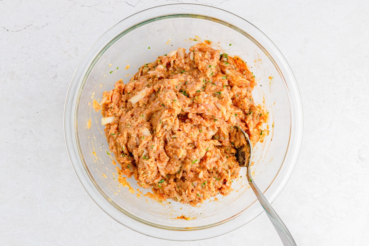 chicken meatloaf mixture in a glass bowl mixed with a spoon in it.