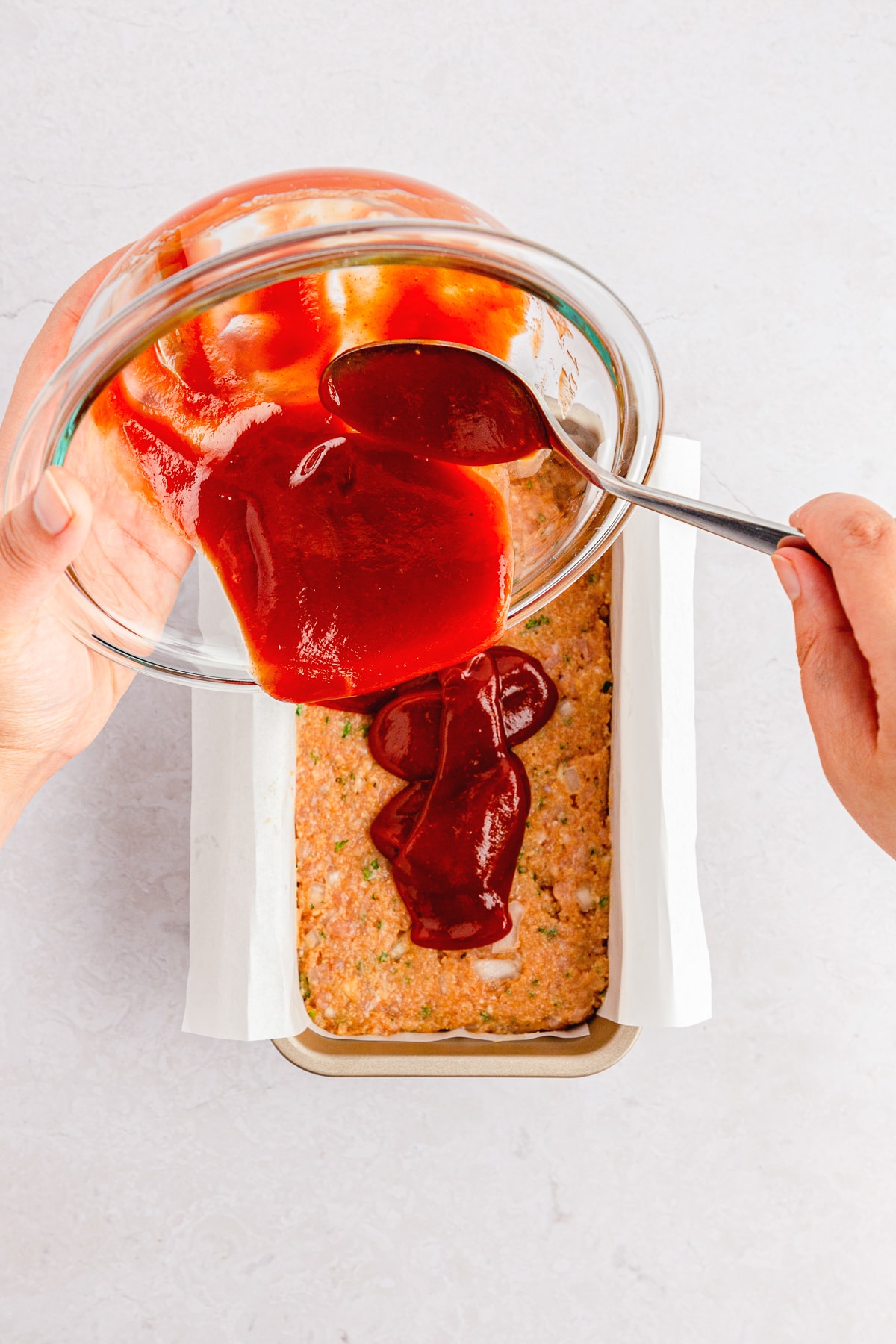 hand holding a bowl of glaze for meatloaf and pouring onto chicken meatloaf in a loaf pan.