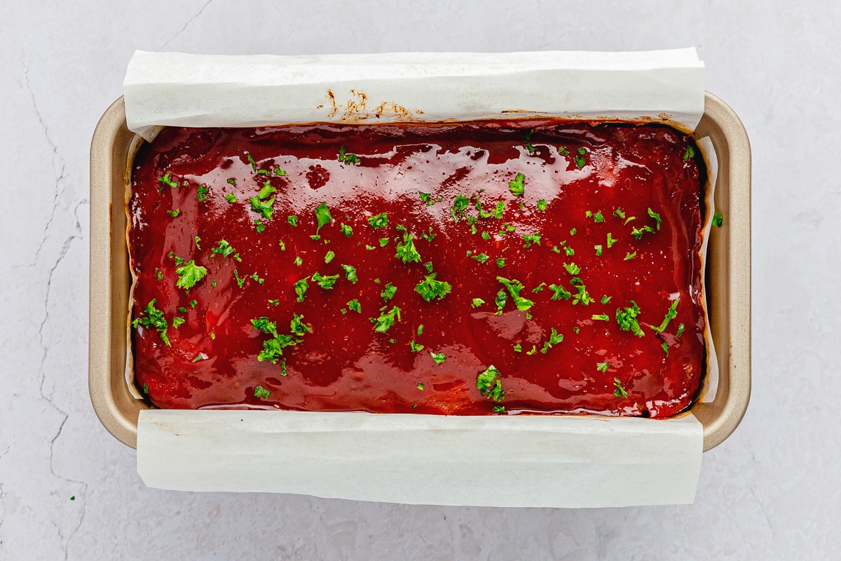 cooked chicken meatloaf garnished with parsley in a loaf pan lined with parchment paper.