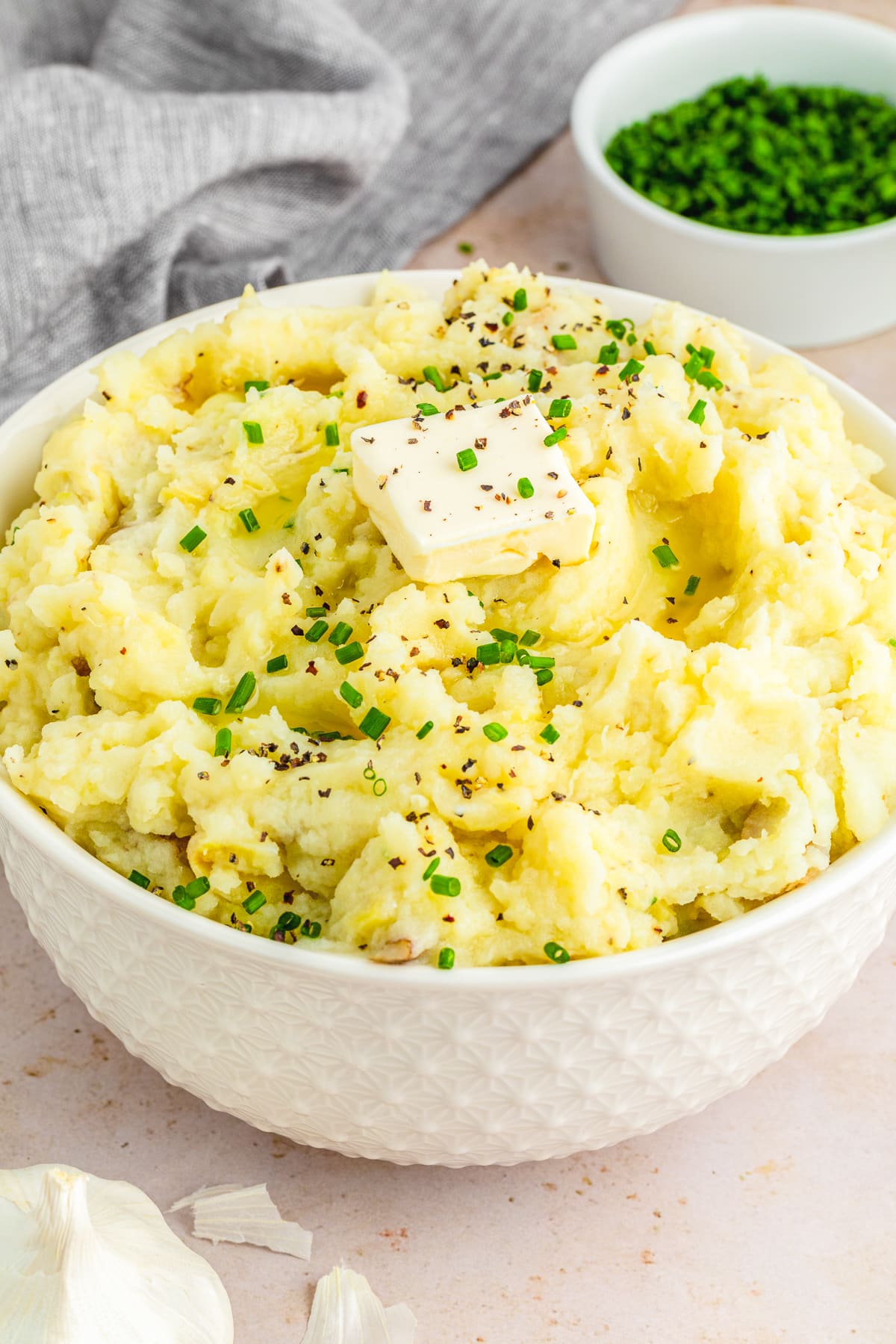 garlic mashed potatoes in a white bowl garnished with butter and chopped chives.