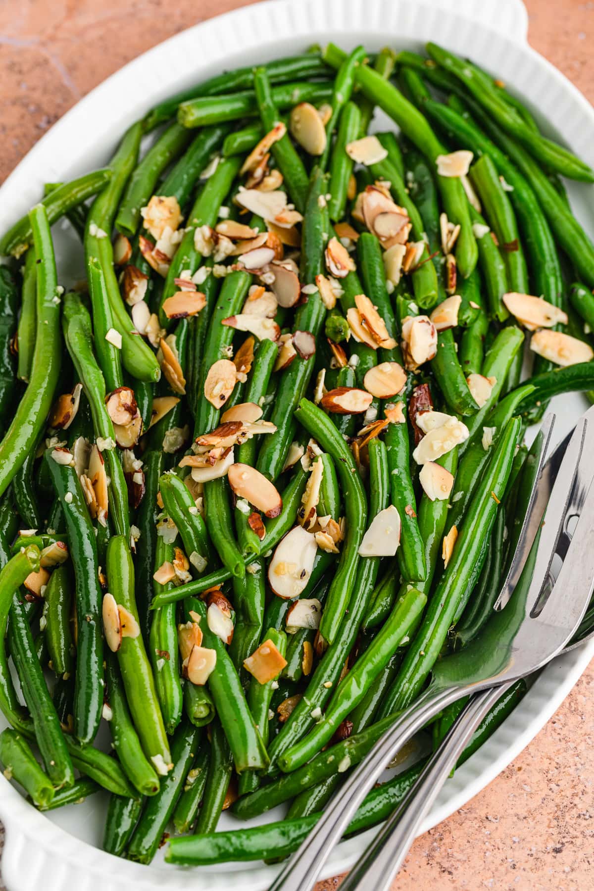 close up of green beans almondine on a white platter with a serving utensils to the side.