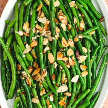overhead photo of green beans almondine on a white platter.