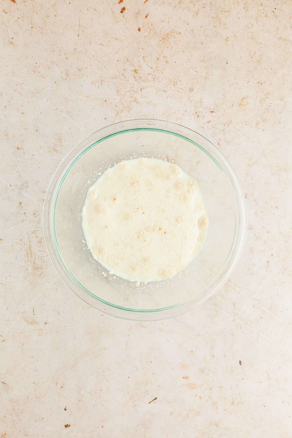 yeast, milk, and sugar in a glass bowl blooming.