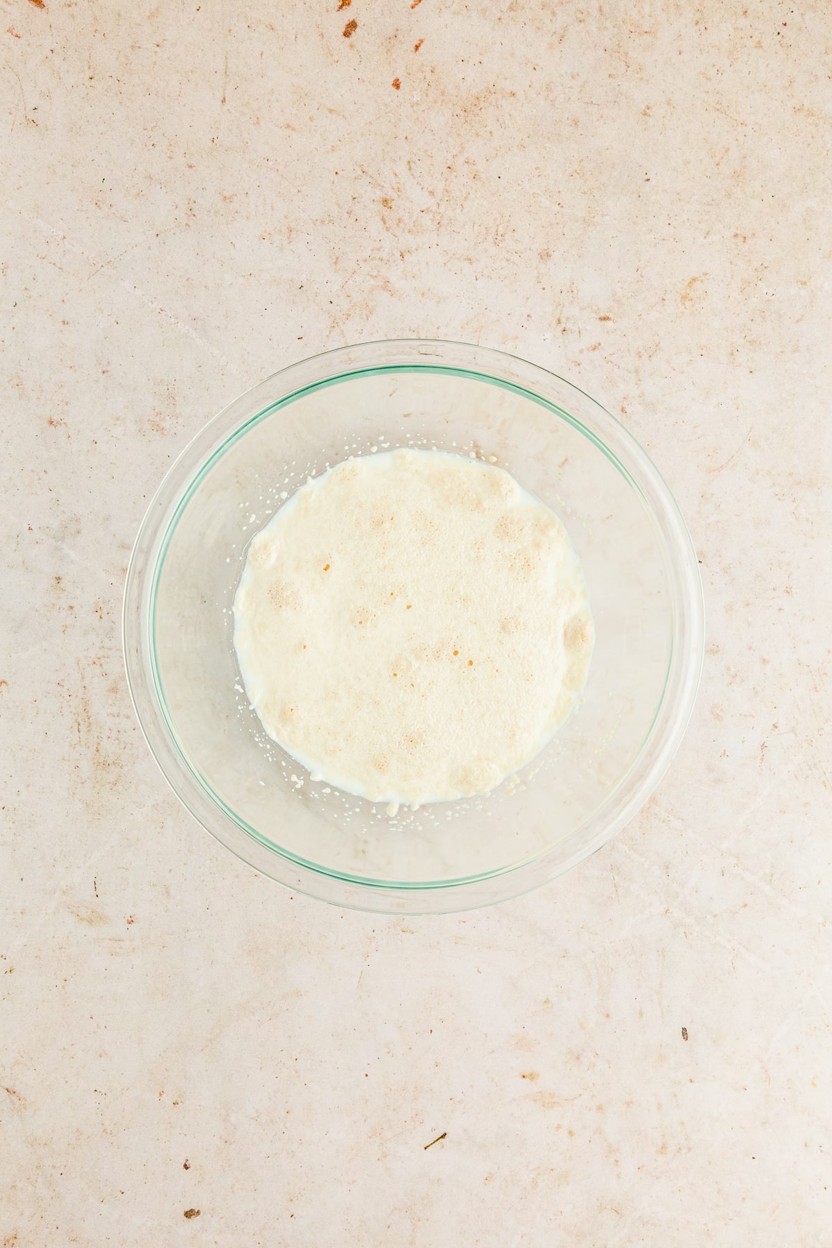 yeast, milk, and sugar in a glass bowl blooming.