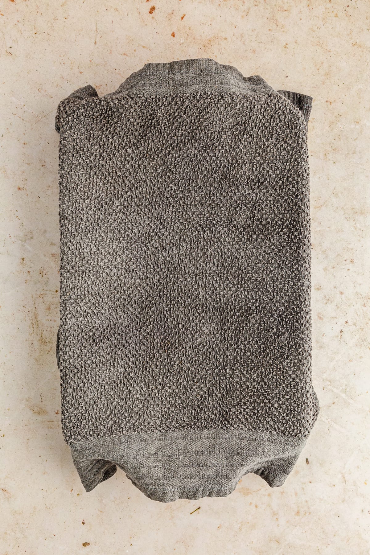 dough rising under a damp gray cloth in a baking dish.