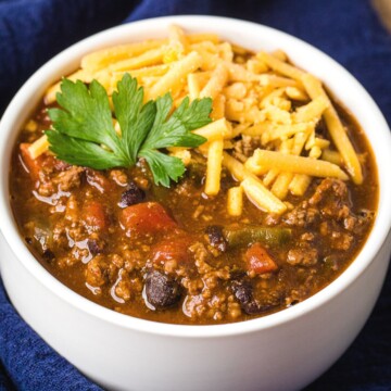 instant pot chili with shredded cheddar and garnish in a white bowl on a navy blue napkin.