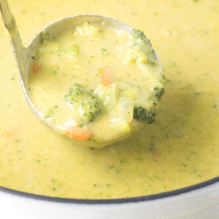 broccoli cheddar soup in a ladle over a dutch oven full of soup.