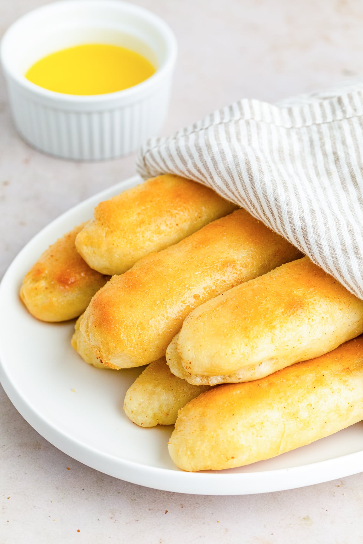 copycat olive garden breadsticks on a plate with a linen napkin ontop of half of them.