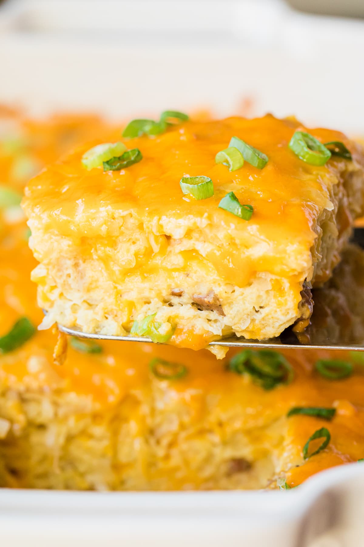 easy breakfast casserole topped with cheese and garnished with green onions on a serving spatula.